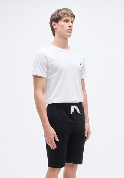 Balti medvilninė trumpomis rankovėmis marškinėliai, derinami su juodais medvilniniais šortais, turinčiais elastingą juosmenį ir baltą raištelį.