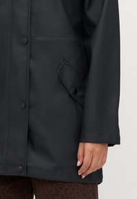 Zwarte waterdichte jas met een gladde textuur, drukknoopsluiting, zijzak met klep en een ontspannen pasvorm.