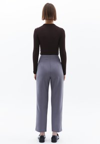 Långärmad brun topp med hög krage, tillsammans med hög midja grå byxor. Outfiten har en skräddarsydd passform och en slät textur.