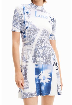Femme portant une robe à manches courtes avec des motifs de cartes et de fleurs bleues et blanches, avec le mot "Love" visible près de l'encolure.