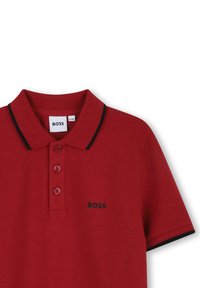 Polo rouge en tissu texturé, trois boutons et accents noirs sur le col et les manches. Présente un logo "BOSS" en noir.
