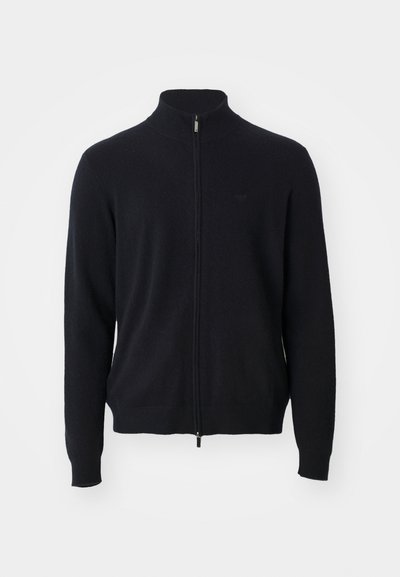 Svart heltäckande zip-tröja med hög krage, långa ärmar och subtil logotyp på vänster bröst, visad mot en vit bakgrund.