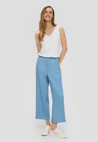 Lichtgewicht, witte katoenen tanktop gecombineerd met loose, lichtblauwe denim culottes. Schoenen zijn beige sneakers met witte zolen.