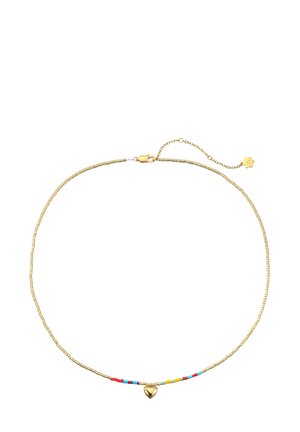 Frau mit goldenen Creolen und einer goldenen Halskette mit bunten Perlen und einem kleinen Herzanhänger, gekleidet in einem weißen Halstertop.