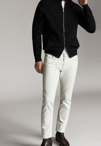 Sweat à capuche noir zippé, jean blanc ajusté, et bottines marron. Tissu lisse et design minimaliste sans motifs ni logos visibles.