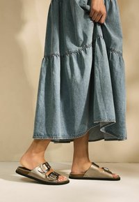 Tan slidesandaler med dubbla metallspännen, matchade med en denimmaxikjol med rynkade våningar och en fransig fåll.