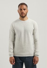 Jersey gris claro con un patrón de punto texturizado, cuello redondo y puños acanalados. Combinado con pantalones de mezclilla oscuros.