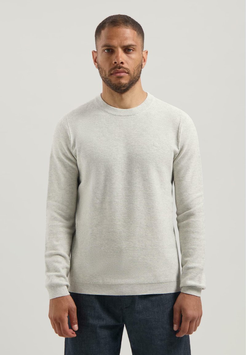 Jersey gris claro con un patrón de punto texturizado, cuello redondo y puños acanalados. Combinado con pantalones de mezclilla oscuros.