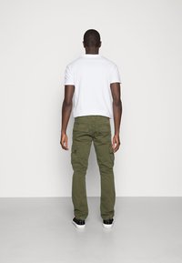 Olivgröna cargobyxor med flera sidofickor, kombinerat med en vit polo med kort ärm. Svartvita sneakers fulländar outfiten.