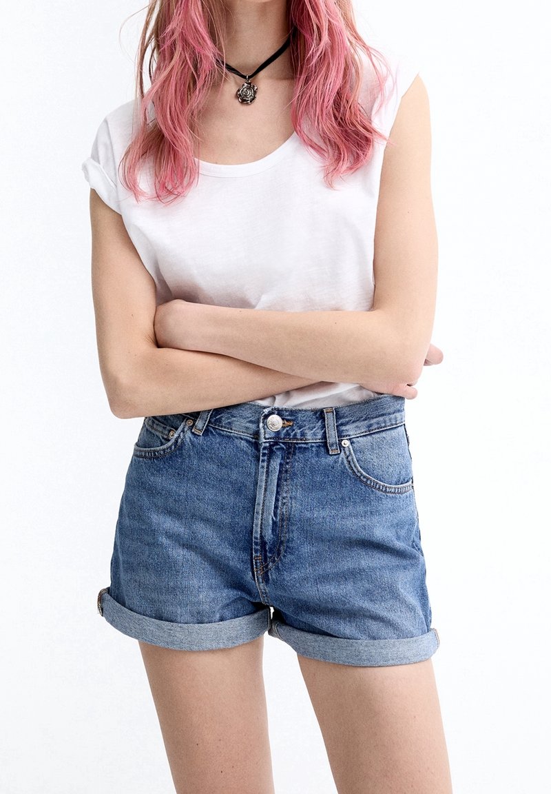 Vaaleansinisen pesun farkkushortsit, joissa ovat käännetyt reunat ja kaksi etutaskua. Yhdistetty valkoiseen lyhythihaiseen t-paitaan. Musta kaulapanta-asuste.