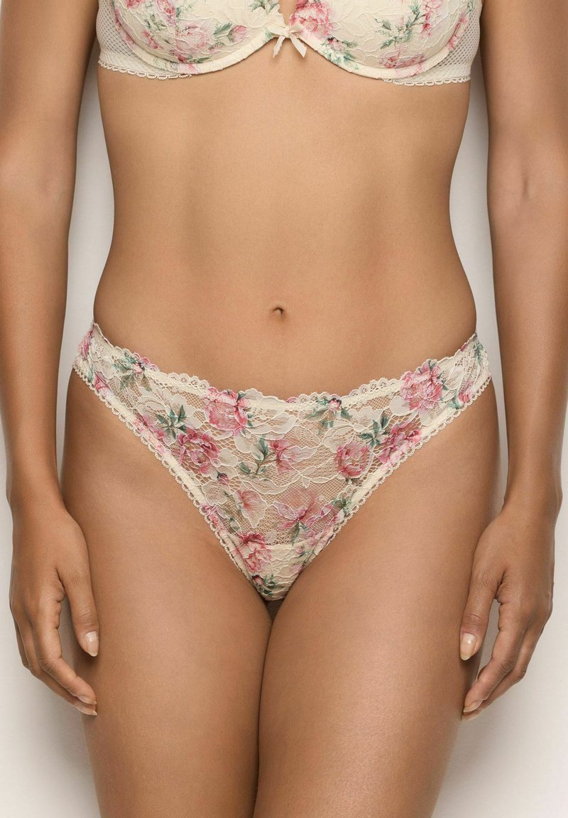 Vrouw in bijpassende beige kanten beha en slip met roze bloemenpatronen, weergegeven van halverwege de torso tot boven de dijen.