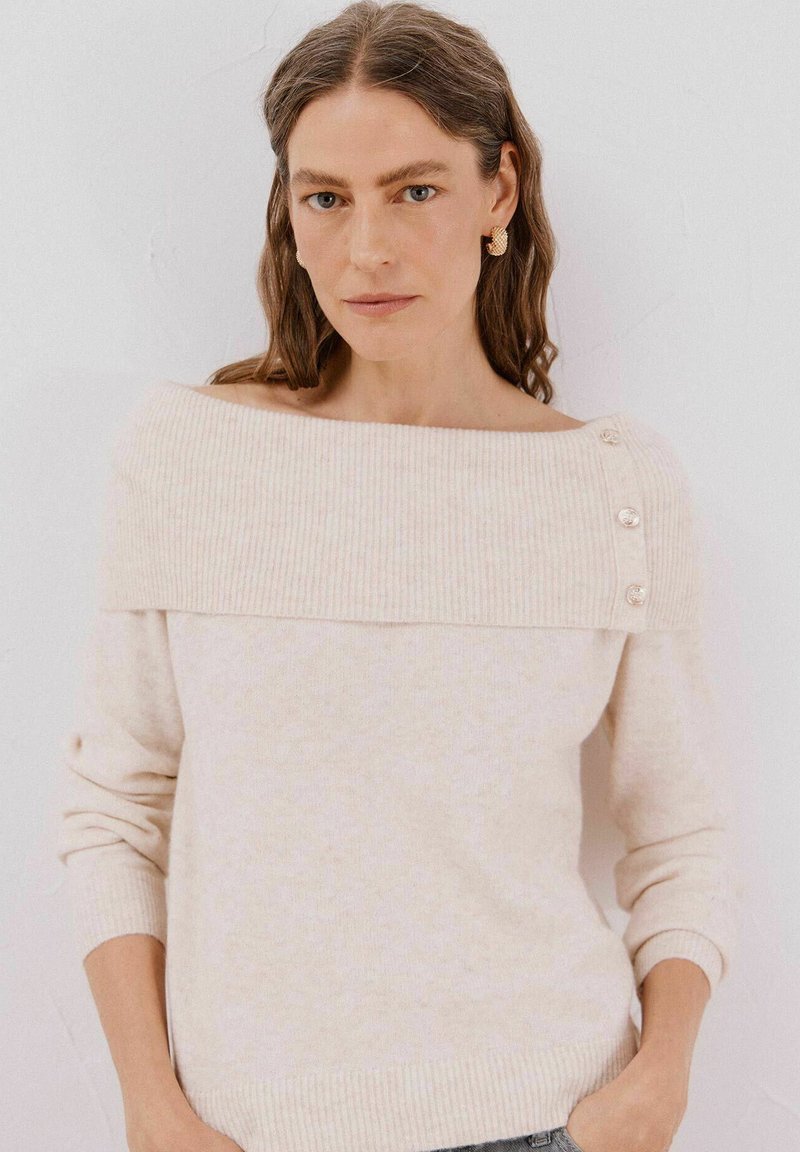 Maglione lavorato a maglia beige chiaro con un design scollato, COLLO a coste e bottoni decorativi sulla spalla sinistra. Texture liscia.