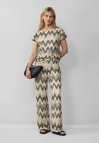 Romige en zwarte zigzagpatroon gebreide top en wijde broek. Een zwarte clutch en platte sandalen maken de outfit compleet.
