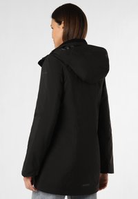 Schwarze wasserdichte Jacke mit Kapuze, die eine glatte Textur, lange Ärmel und knöpfbare Manschetten hat, von hinten gezeigt.
