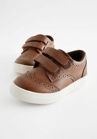 Zapatos de cuero marrón con dos tiras de Velcro, diseño perforado y suela de goma blanca. Presentan una punta redondeada y una forma de perfil bajo.