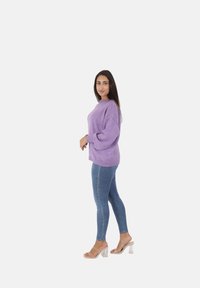Maglione in maglia viola con collo alto e maniche a palloncino, abbinato a jeans aderenti in denim e sandali trasparenti con tacco.