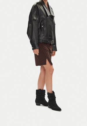 Czarna skórzana, oversize'owa kurtka, brązowa spódnica do kolan oraz czarne zamszowe botki na niewielkim obcasie. Kurtka ma pasek i skręcone mankiety przy botkach.