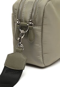 Borsa rettangolare in nylon verde chiaro, morbida al tatto, con zip argentate. Presenta un attacco per la tracolla in pelle e una tracolla nera a contrasto.