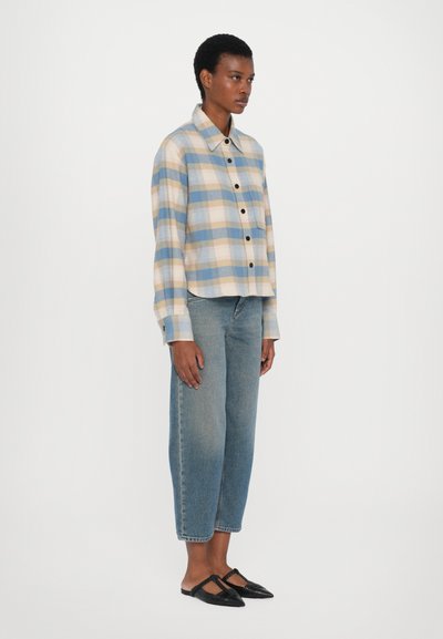Lyseblå rutete skjorte med mørke knapper, spiss krage og lange ermer, kombinert med tettsittende blå denimjeans og sorte slip-on sko.