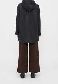 Zwarte gewatteerde jas met een losse pasvorm, gladde textuur en lange mouwen, gecombineerd met bruine wijde broekspijpen met een subtiele luipaardprint.