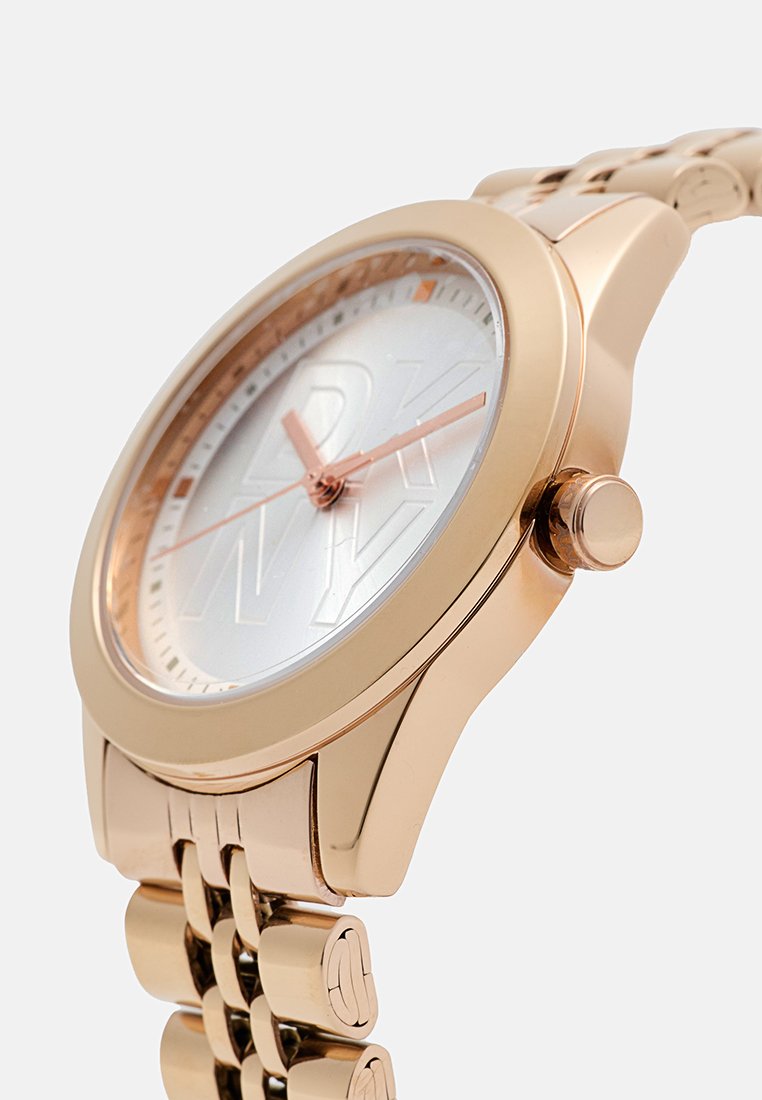 Rose-Gold-Uhr mit rundem Gehäuse, weißem strukturiertem Zifferblatt, roségoldenen Zeigern und Metallarmband. Mit einem Logo in der Mitte.