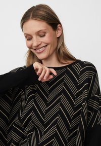 Zwarte gebreide poncho met een diagonaal chevronpatroon in metallic goud. Geribde manchetten en een brede halslijn maken het ontwerp compleet.