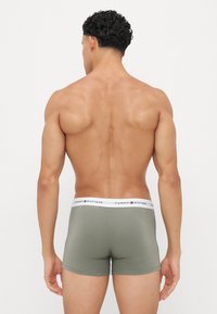 Groene boxershorts met een witte tailleband waarop "TOMMY HILFIGER" staat. De stof lijkt glad en aansluitend, met een strakke pasvorm.