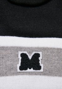 Pletený sveter s čiernymi, šedými a bielymi horizontálnymi pruhmi. Obsahuje štruktúrovanú čiernu nášivku s logom orámovanú bielou. Mäkká textúra.