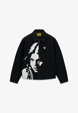 Veste noire zippée avec un graphisme blanc du visage d'une femme sur le devant et un petit logo triangulaire sur la poitrine.