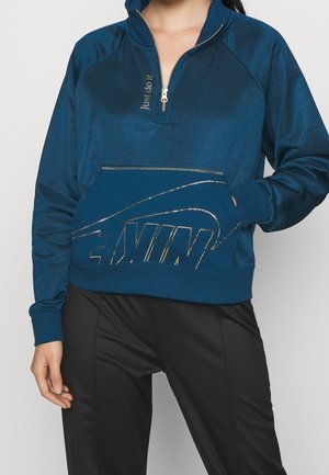 Blå zip-tröja med metalliceffekt och detaljer. Har en framfick i känguru-stil och ribbade ärmslut. Bärs med svarta byxor.