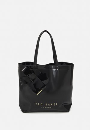 Czarna torba Tote Ted Baker London z lakierowanym wykończeniem, ozdobną kokardą i podwójnymi paskami na ramię na jednolitym tle.