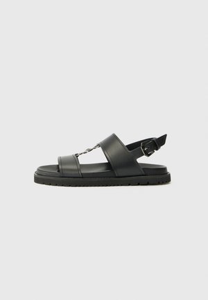 Black leather sandals with two wide straps, a chain accent, and adjustable buckle on the heel. Lightweight sole with textured tread.