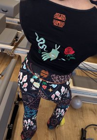 Zwarte top met kleurrijke geborduurde ontwerpen, met een hand, slang en roos. Levendige legging met diverse patronen in meerdere kleuren.