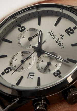 Montre analogique argentée avec accents noirs, trois sous-cadrans, grands chiffres, boîtier en acier inoxydable et affichage de la date à 6 heures.