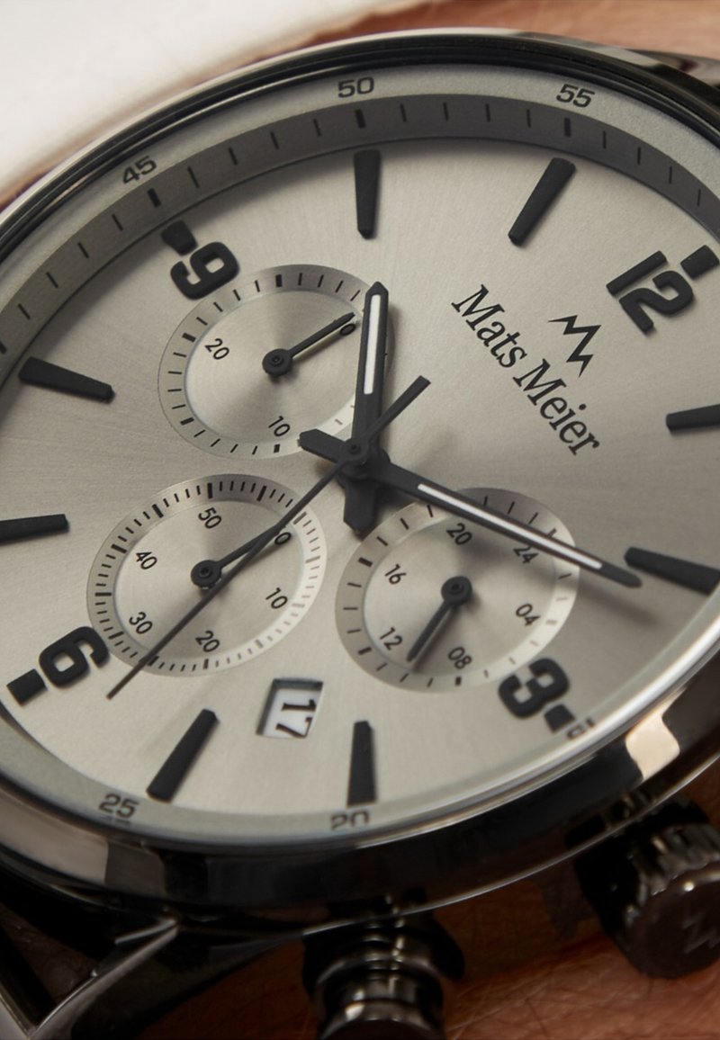 Montre analogique argentée avec accents noirs, trois sous-cadrans, grands chiffres, boîtier en acier inoxydable et affichage de la date à 6 heures.