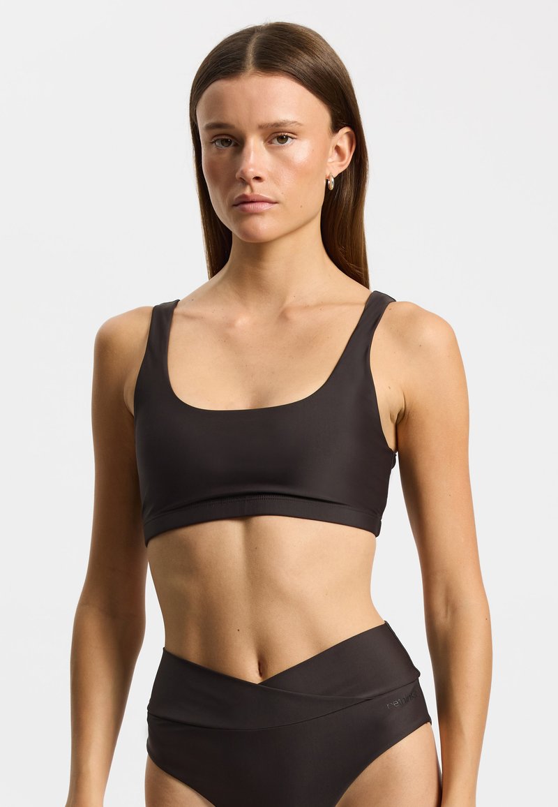 Brassière de sport noire avec un décolleté carré et de larges bretelles, en matière lisse. Associée à un bas de bikini noir taille haute avec un design enveloppant.
