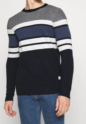 Pull en maille bleu marine avec des rayures horizontales grises, blanches et bleu clair, avec des poignets et un ourlet côtelés, étiquette visible en bas.