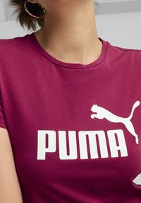 Vínová bavlněná tričko s bílým logem "PUMA" a grafikou skákajícího kočky, kulatým výstřihem a krátkými rukávy.