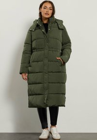 Lang grøn pufferjakke med trykknapper, sidelommer og aftagelig hætte, med en quiltet tekstur og i midt-længer.
