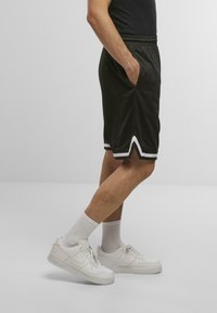Fekete sportnadrág fehér oldalsávokkal, rugalmas derékrésszel és oldalsó zsebekkel, fehér sportcipőkkel és bokazoknival párosítva.