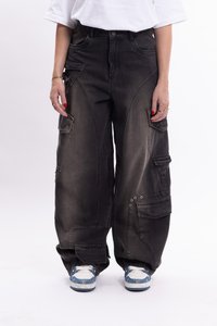 Pantalones cargo de mezclilla negra con múltiples bolsillos, corte holgado y detalles metálicos. Llevados con zapatillas de deporte de patrón azul y blanco.