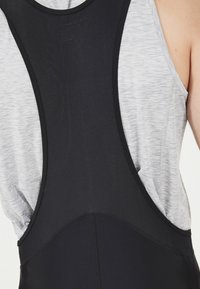 Czarny sportowy top na ramiączkach z tylnym wycięciem, z oddychającego materiału siatkowego o gładkiej fakturze. Szary akcent z przodu.