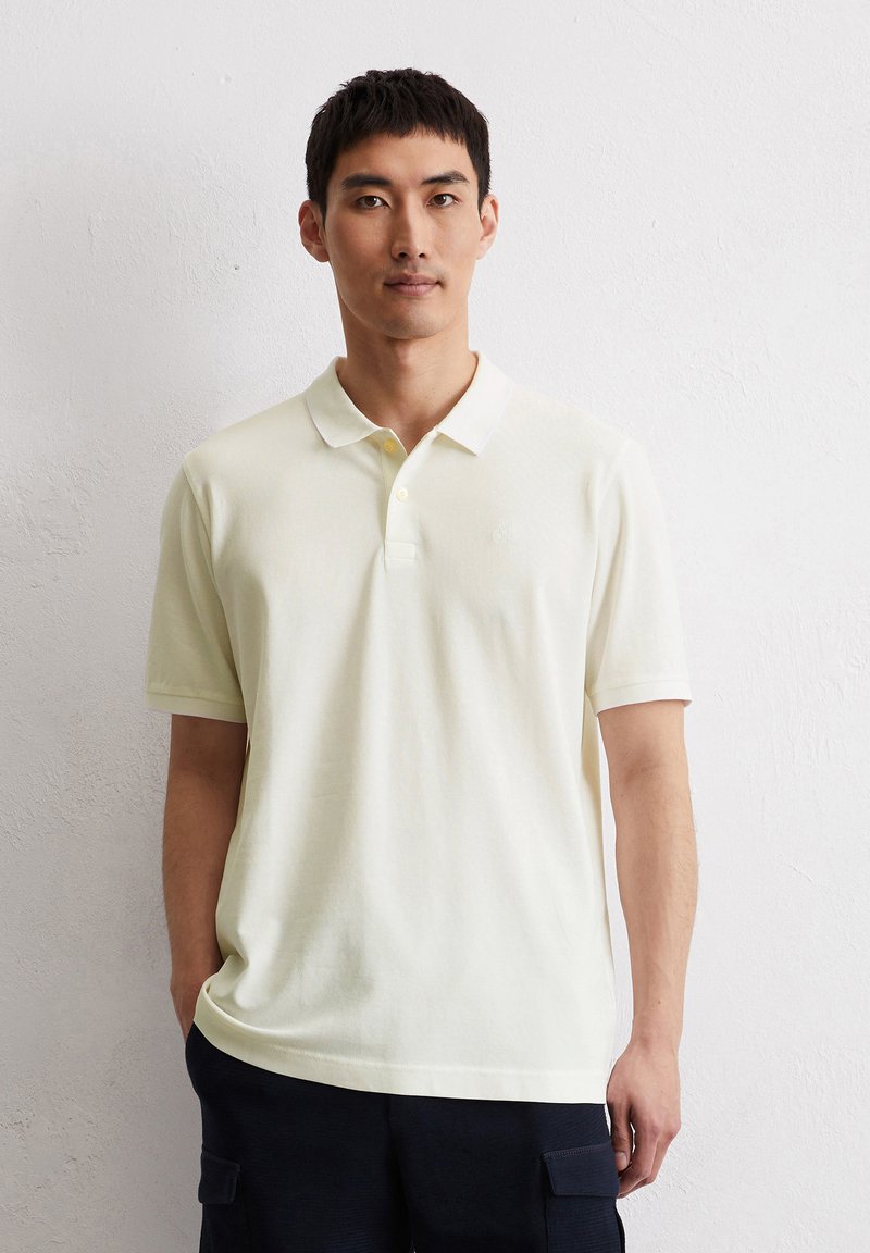 Pale yellow polo shirt made of soft fabric, featuring a classic collar, three-button placket, and subtle logo on the chest.