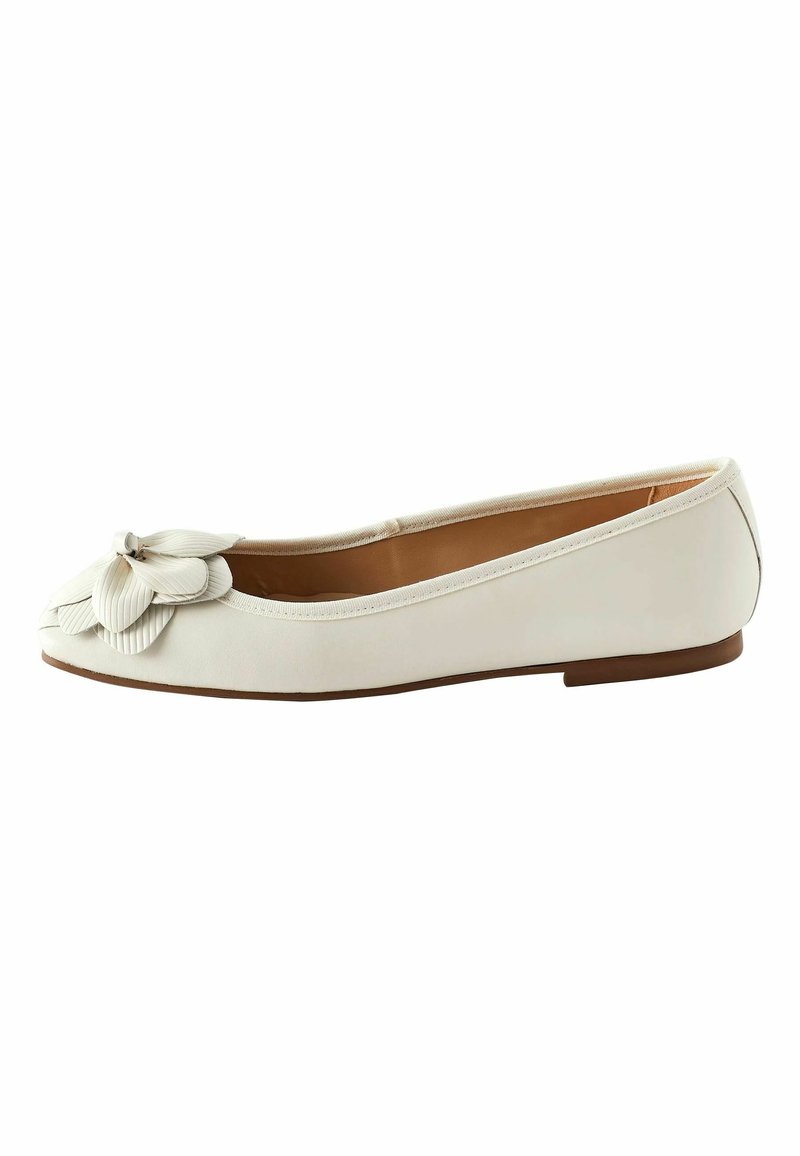 Chaussure de ballet plate blanche avec un bout rond et un détail floral superposé décoratif à l'avant, et une semelle basse marron.