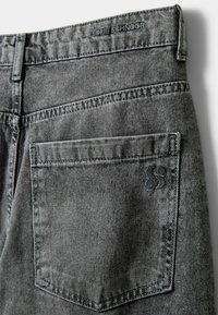 Sive džins hlače z teksturirano površino, ki vključujejo zadnji žep in embosirano blagovno znamko. Šivanje podrobnosti vzdolž šivov.