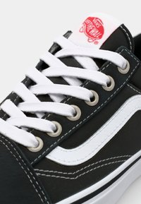 Schwarze Canvas-Sneaker mit weißen Schnürsenkeln und Nähten, ausgestattet mit einem weißen Seitenstreifen und runden silbernen Ösen. Rotes Logo auf der Zunge.