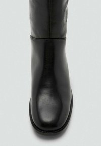 Bottine en cuir noir avec une texture lisse. Bout arrondi et design épuré. Coutures discrètes le long des joints et semelle plate.