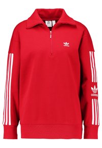 Röd sweatshirt med hög krage, zip fram, vitt Adidas-logotyp och tre vita ränder på varje ärm. Mjuk tygtextur.