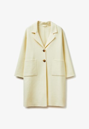 Abrigo largo color crema con cuello con muesca, dos botones marrones, dos grandes bolsillos frontales y mangas de tres cuartos.