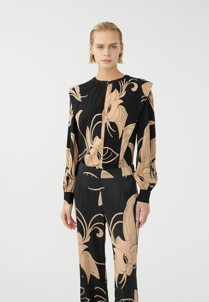 Schwarze Bluse mit beigem Blumenmuster, mit einem leichten Rüschendetail an den Schultern, langen Ärmeln und einer Knopfleiste vorne. Glatte Stoffstruktur.